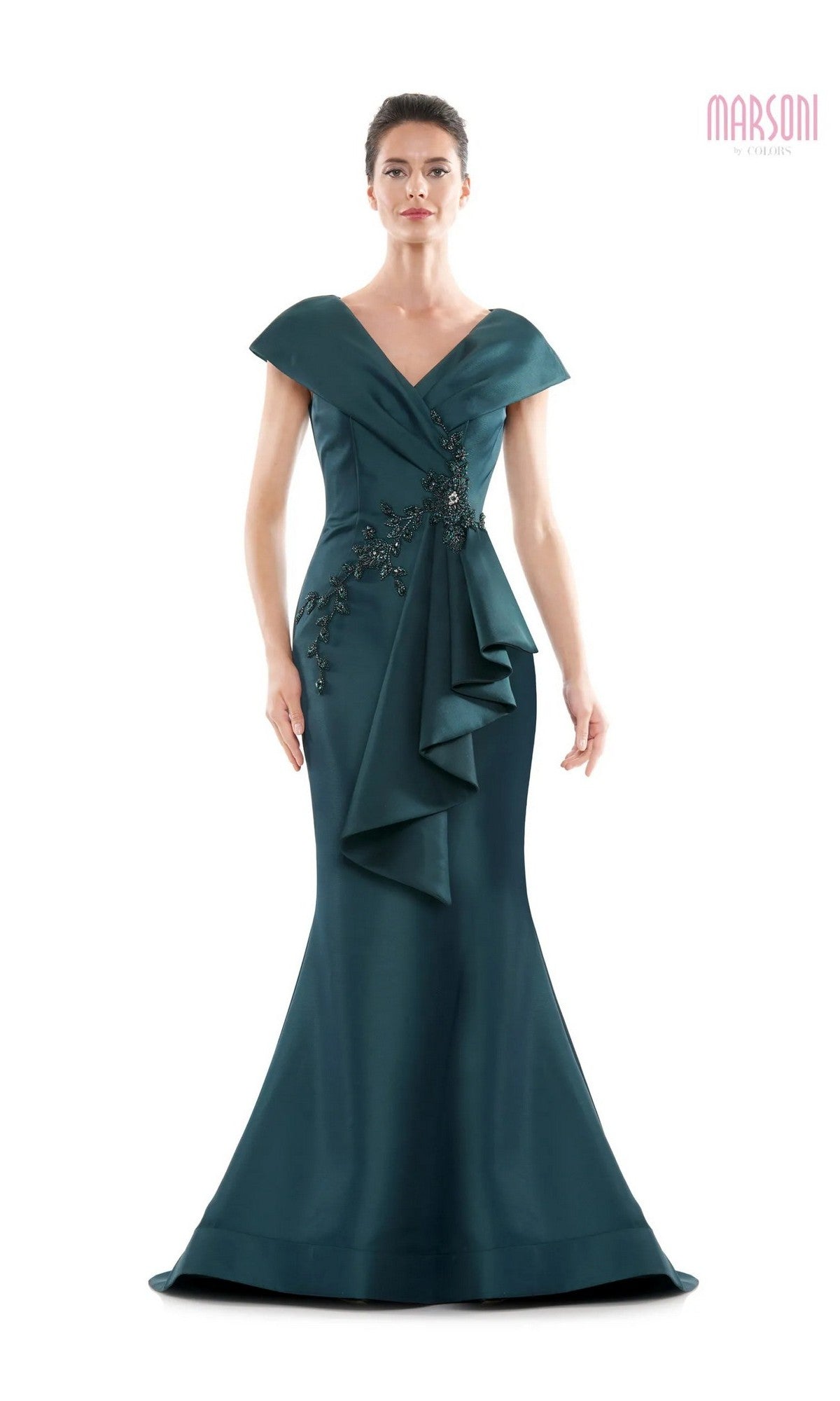 A woman wearing the Marsoni MV1086 long formal dress in deep green, featuring an off-the-shoulder neckline, floor-length trumpet silhouette, floral embellishments, and cascading front ruffle detail.